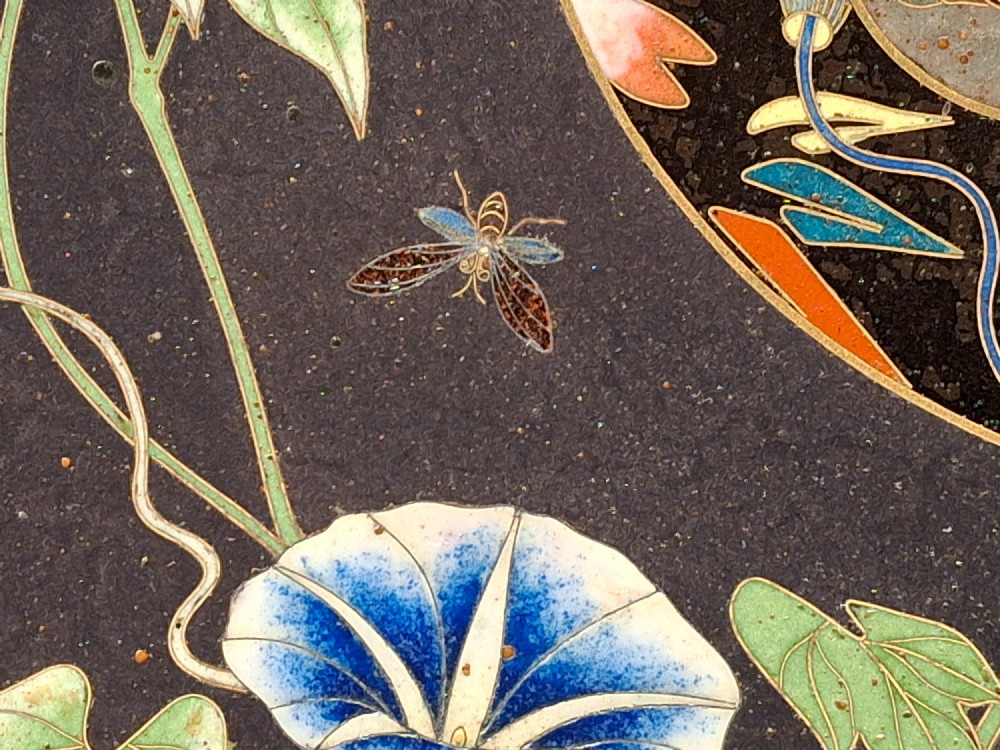 A circular Japanese cloisonne enamel plate featuring intricate floral, landscape, and geometric designs in blue, green, and red against a dark ground. View III