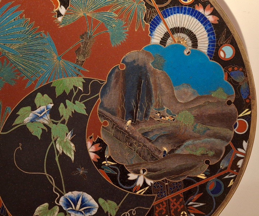 A circular Japanese cloisonne enamel plate featuring intricate floral, landscape, and geometric designs in blue, green, and red against a dark ground. View IV