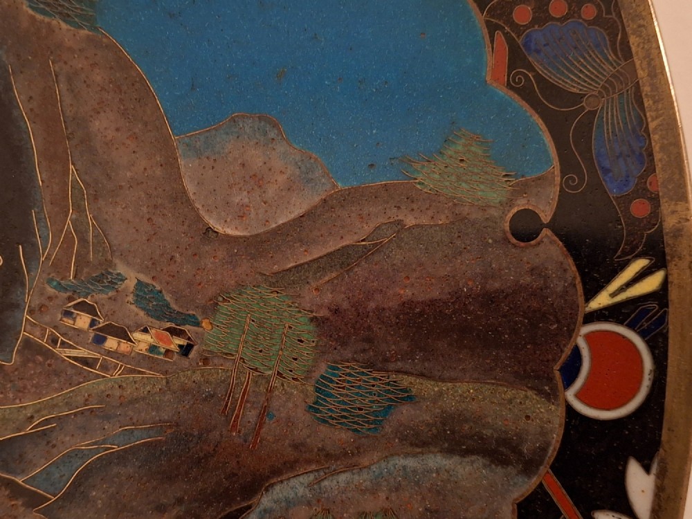 A circular Japanese cloisonne enamel plate featuring intricate floral, landscape, and geometric designs in blue, green, and red against a dark ground. View VII