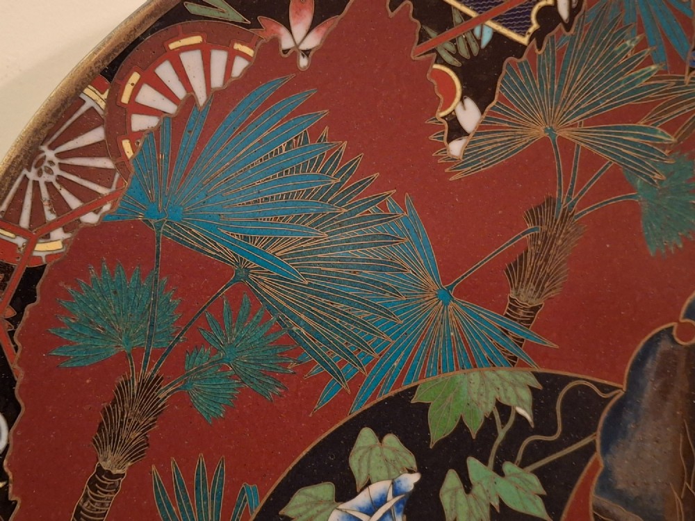A circular Japanese cloisonne enamel plate featuring intricate floral, landscape, and geometric designs in blue, green, and red against a dark ground. View IX