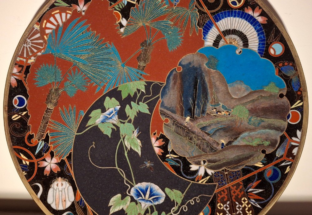 A circular Japanese cloisonne enamel plate featuring intricate floral, landscape, and geometric designs in blue, green, and red against a dark ground. View X