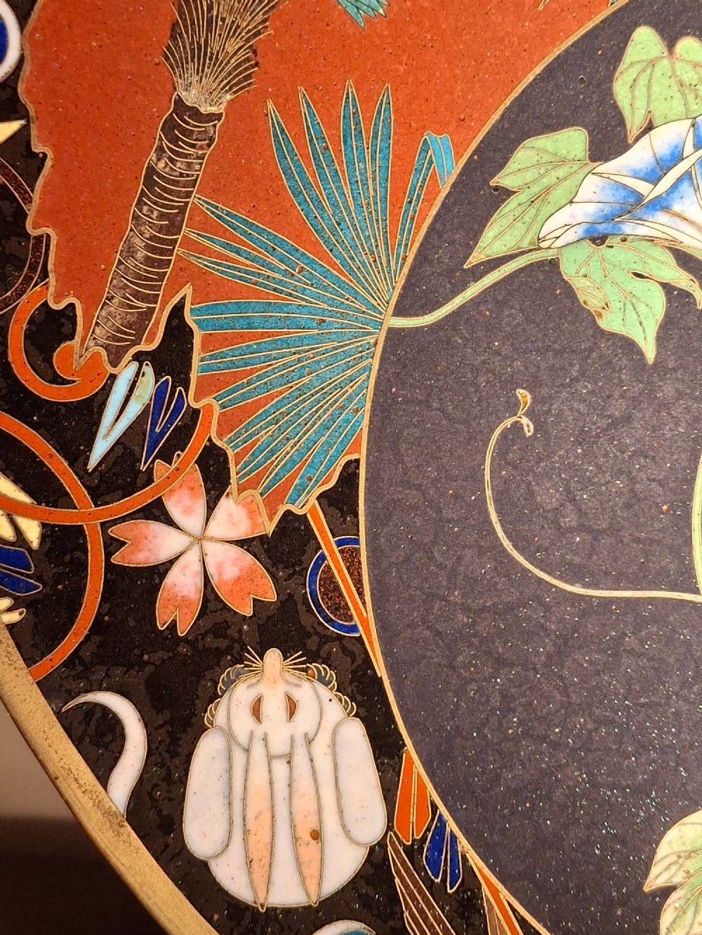 A circular Japanese cloisonne enamel plate featuring intricate floral, landscape, and geometric designs in blue, green, and red against a dark ground. View XIII