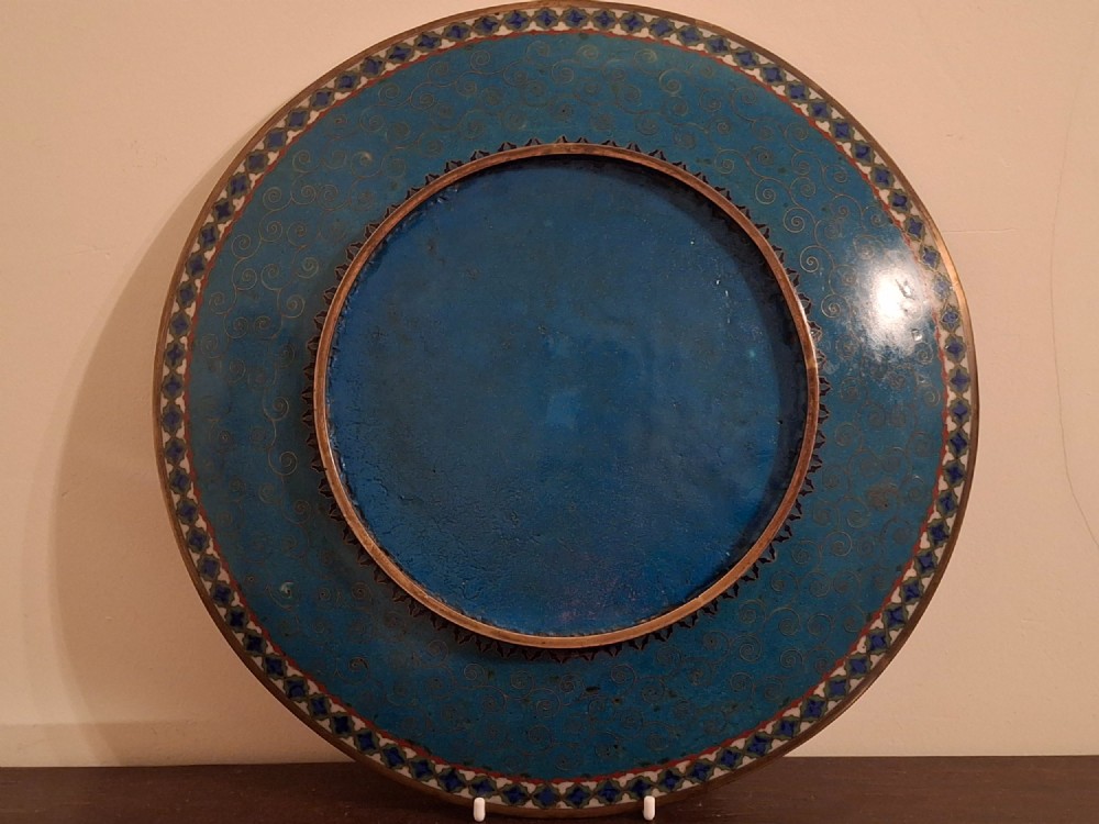 A circular Japanese cloisonne enamel plate featuring intricate floral, landscape, and geometric designs in blue, green, and red against a dark ground. View XIV