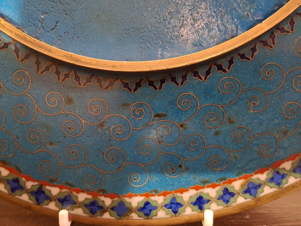 A circular Japanese cloisonne enamel plate featuring intricate floral, landscape, and geometric designs in blue, green, and red against a dark ground. View XV