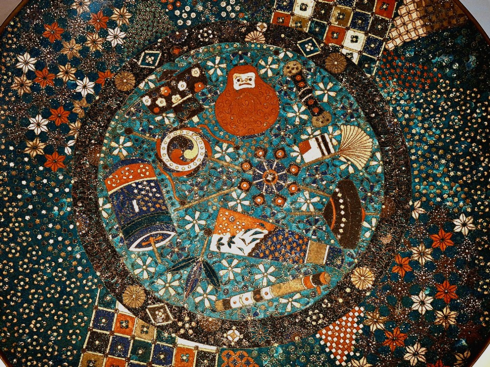 A circular Japanese cloisonne charger featuring a central blue medallion with a red Daruma figure surrounded by detailed geometric and floral patterned borders. View IV