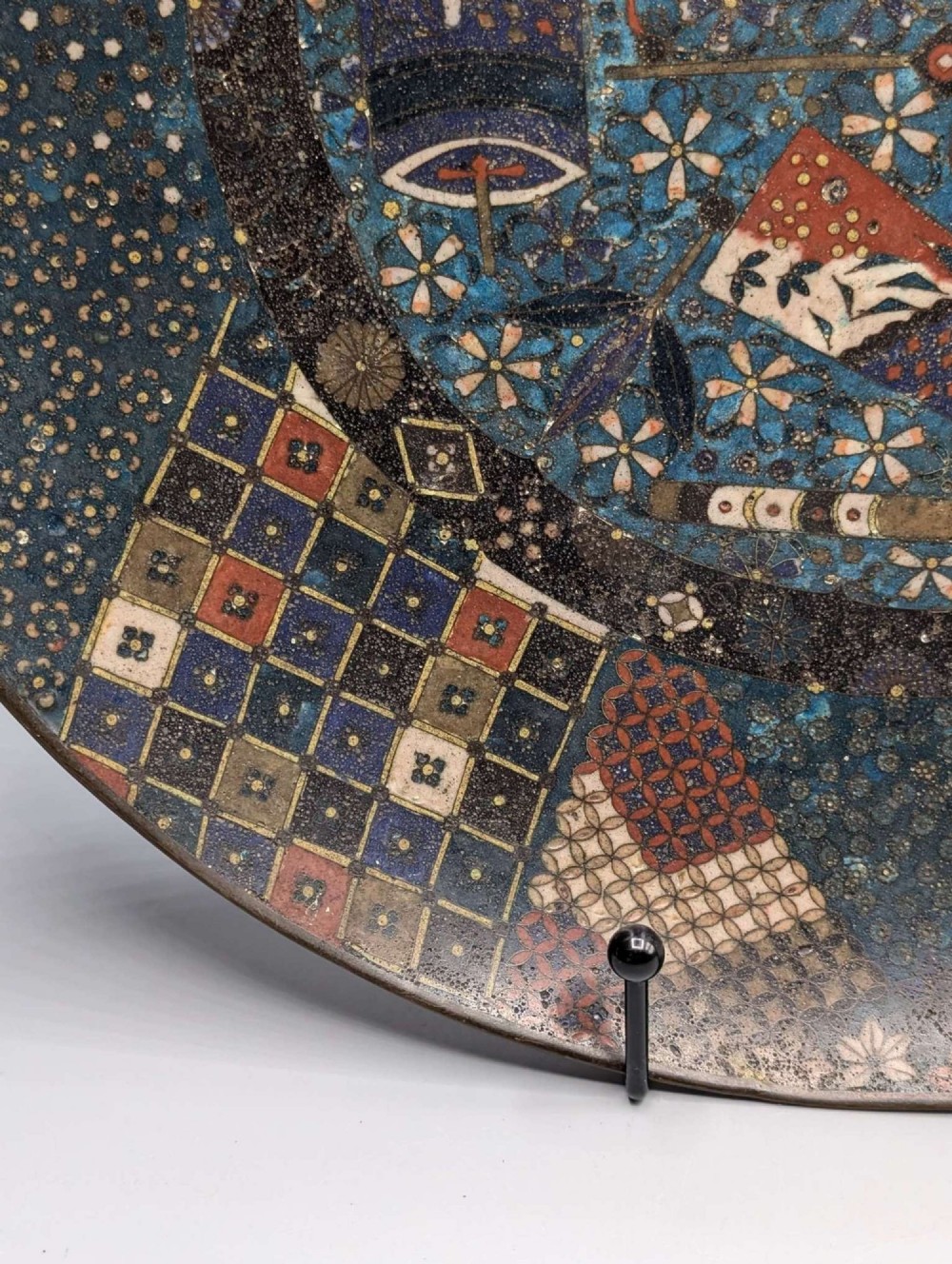 A circular Japanese cloisonne charger featuring a central blue medallion with a red Daruma figure surrounded by detailed geometric and floral patterned borders. View VII
