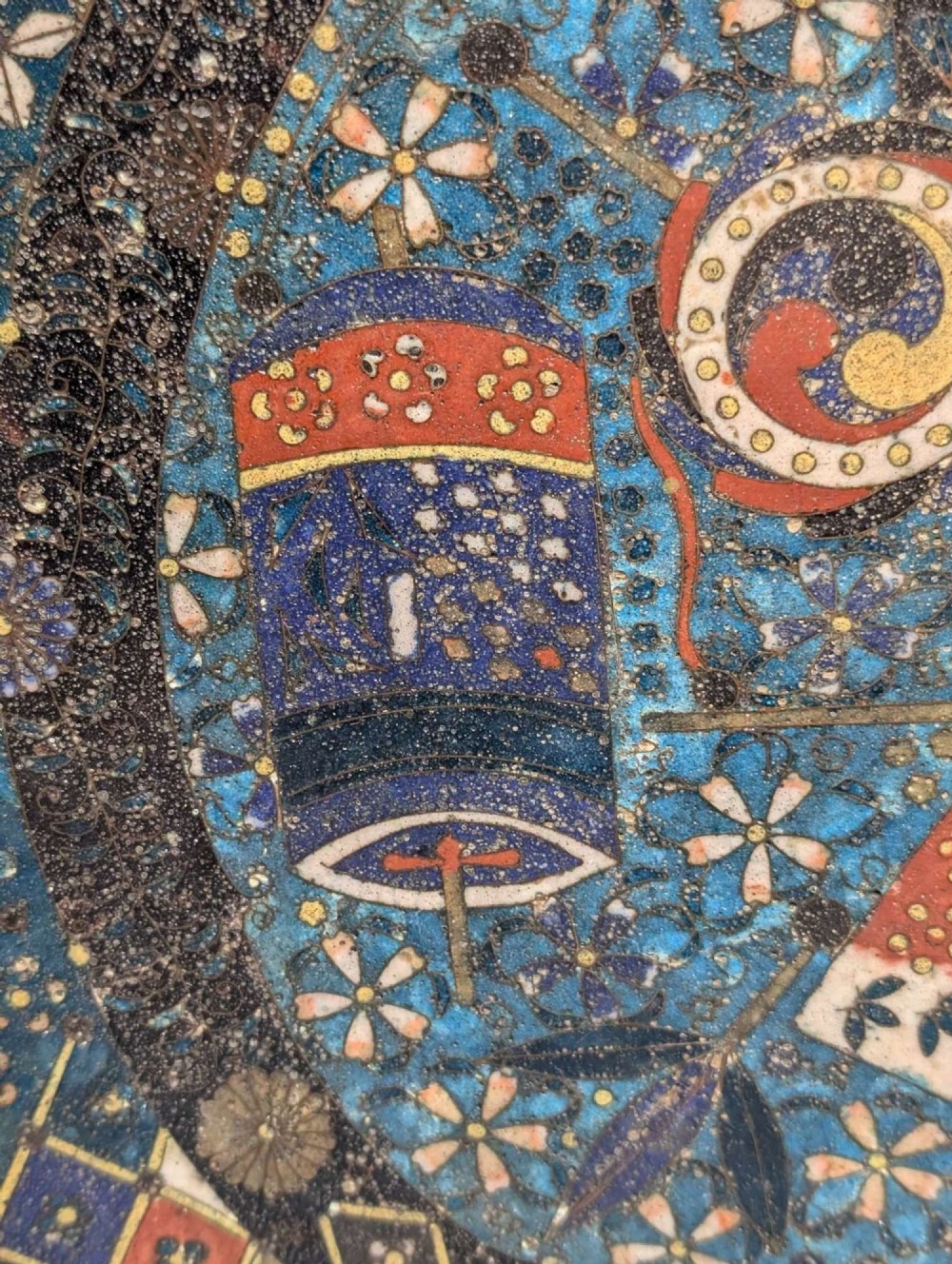 A circular Japanese cloisonne charger featuring a central blue medallion with a red Daruma figure surrounded by detailed geometric and floral patterned borders. View XI