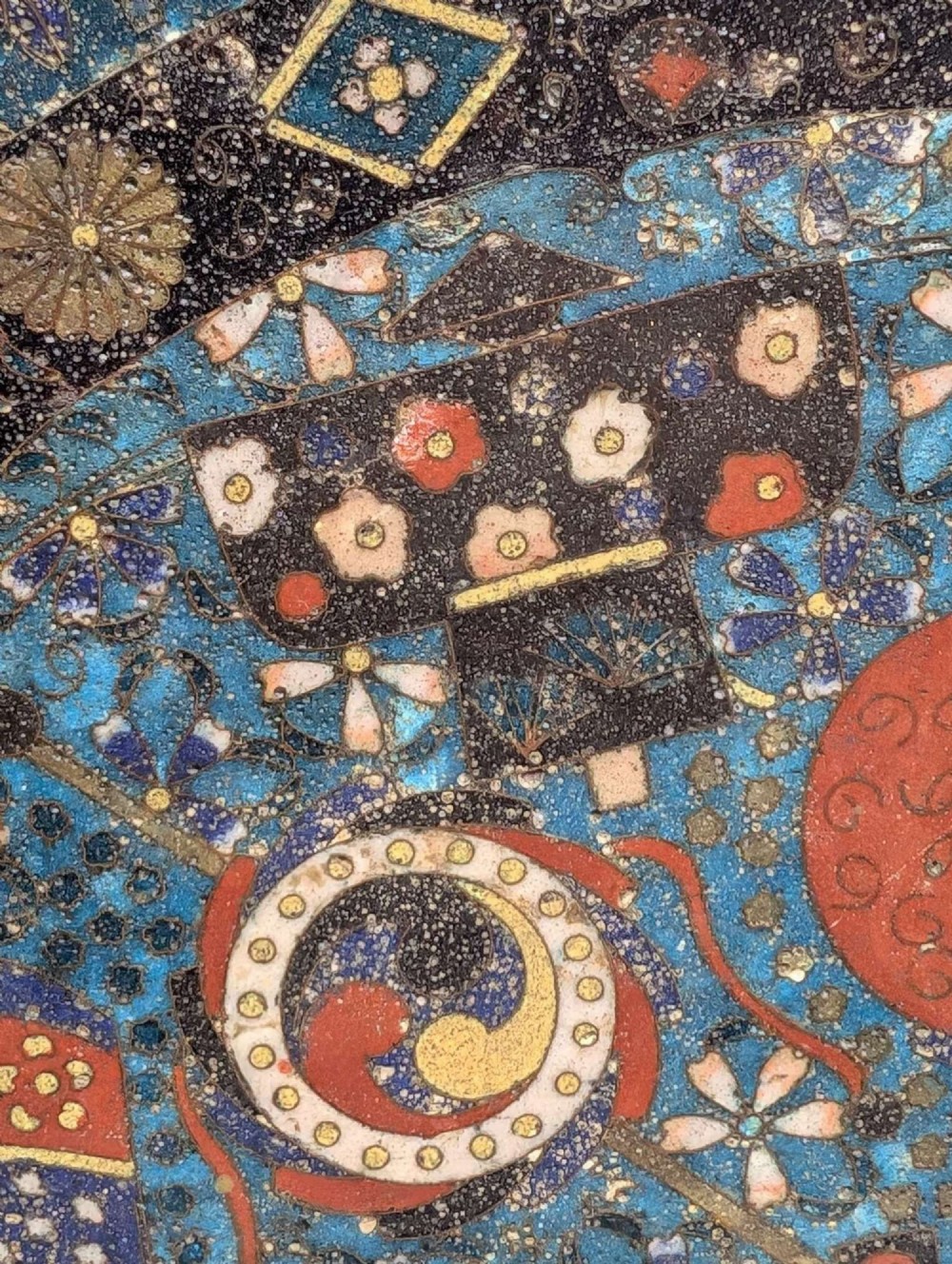 A circular Japanese cloisonne charger featuring a central blue medallion with a red Daruma figure surrounded by detailed geometric and floral patterned borders. View XII
