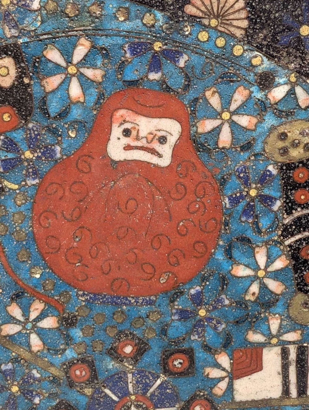A circular Japanese cloisonne charger featuring a central blue medallion with a red Daruma figure surrounded by detailed geometric and floral patterned borders. View XIII
