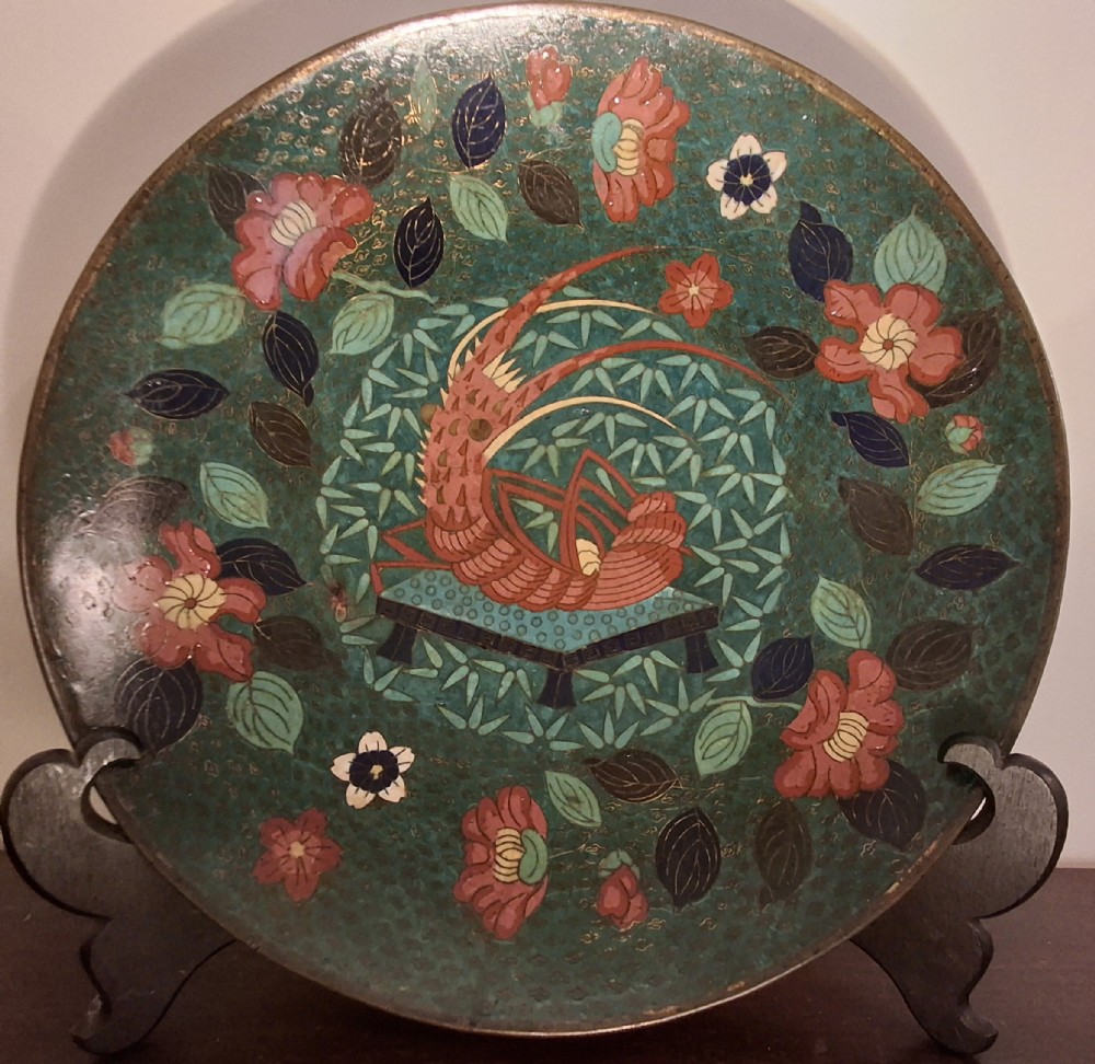 A circular Japanese cloisonne enamel charger displaying an orange shrimp motif surrounded by red flowers on a teal green pattern background. View X