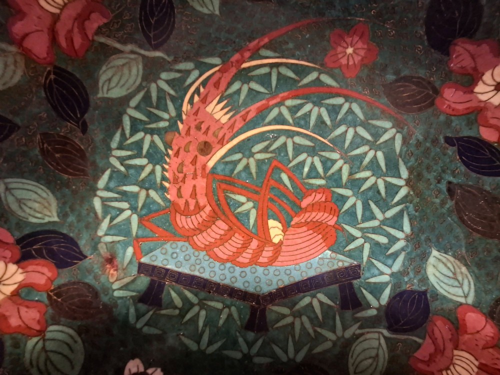 A circular Japanese cloisonne enamel charger displaying an orange shrimp motif surrounded by red flowers on a teal green pattern background. View XI