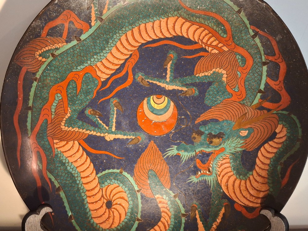 A circular Japanese Meiji period cloisonne enamel charger featuring a green and terracotta coiling dragon surrounding a flaming pearl on a dark blue background. View V