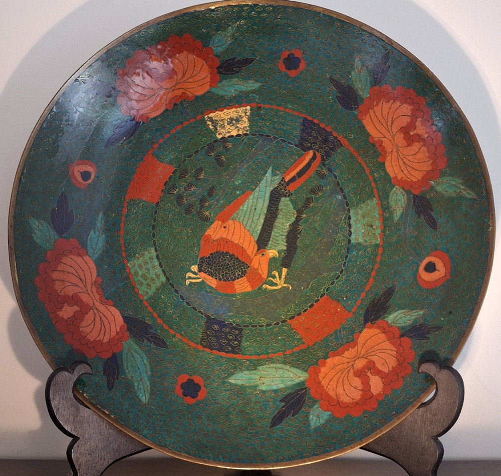 A circular antique Japanese cloisonne charger featuring a central bird motif surrounded by large orange peony blossoms on a green patterned enamel ground.