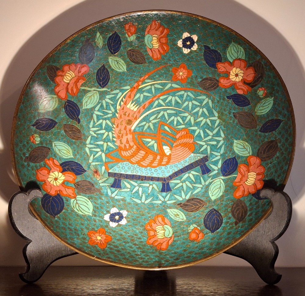A circular Japanese cloisonne enamel charger displaying an orange shrimp motif surrounded by red flowers on a teal green pattern background.