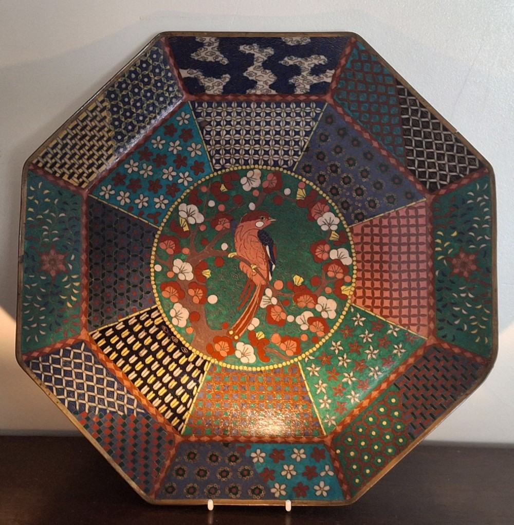 An octagonal antique Japanese cloisonne enamel tray featuring a central bird on a flowering branch surrounded by colourful geometric brocade panels.