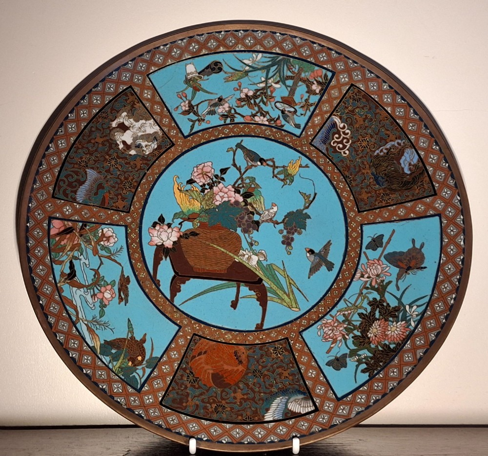 A circular Japanese cloisonne enamel charger featuring a central turquoise medallion with a floral vase and birds, enclosed by patterned borders and surrounding nature panels.