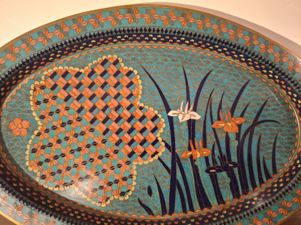 An oval Japanese cloisonne enamel tray featuring a turquoise background decorated with blue and orange iris flowers alongside geometric lattice patterns. View VI