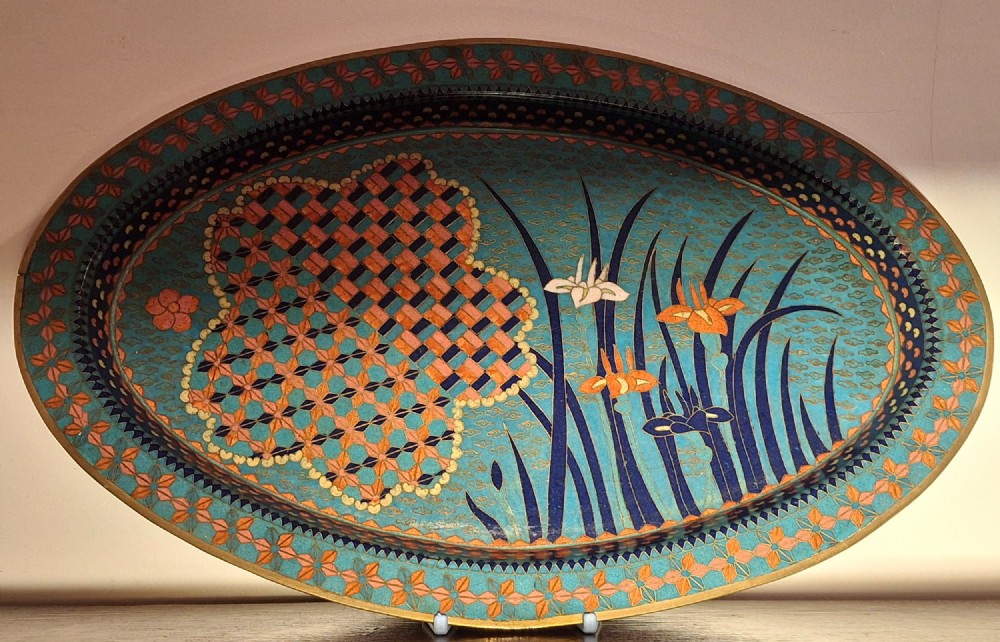 An oval Japanese cloisonne enamel tray featuring a turquoise background decorated with blue and orange iris flowers alongside geometric lattice patterns.