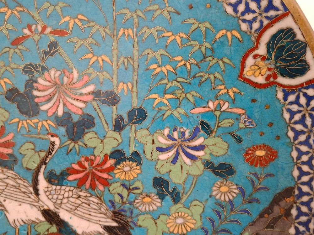 A circular Japanese cloisonne enamel decorative plate decorated with two wading birds surrounded by flowers against a turquoise ground with an ornamental geometric border. View III