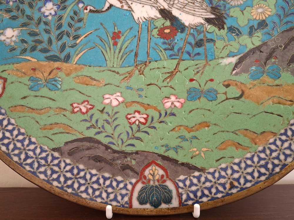 A circular Japanese cloisonne enamel decorative plate decorated with two wading birds surrounded by flowers against a turquoise ground with an ornamental geometric border. View V