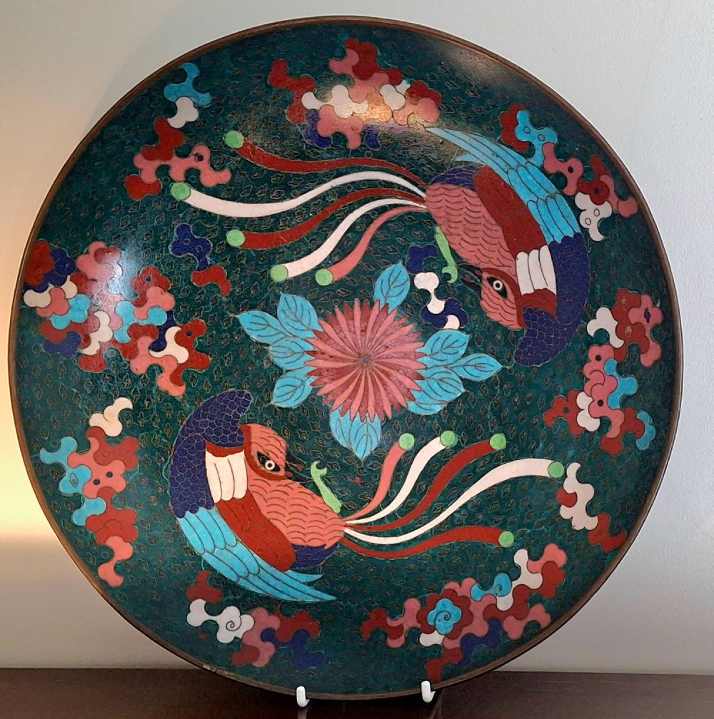 A circular antique Japanese cloisonne enamel charger decorated with two colourful Ho-o phoenix birds and a central floral chrysanthemum motif against a dark teal pattern.
