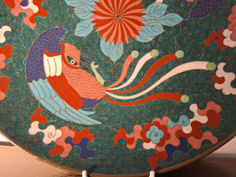 A circular antique Japanese cloisonne enamel charger decorated with two colourful Ho-o phoenix birds and a central floral chrysanthemum motif against a dark teal pattern. View X