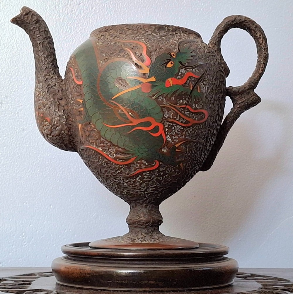 A Japanese Totai Shippo teapot with a textured tree-bark surface and green enamel dragon decoration, resting on a carved wooden base.