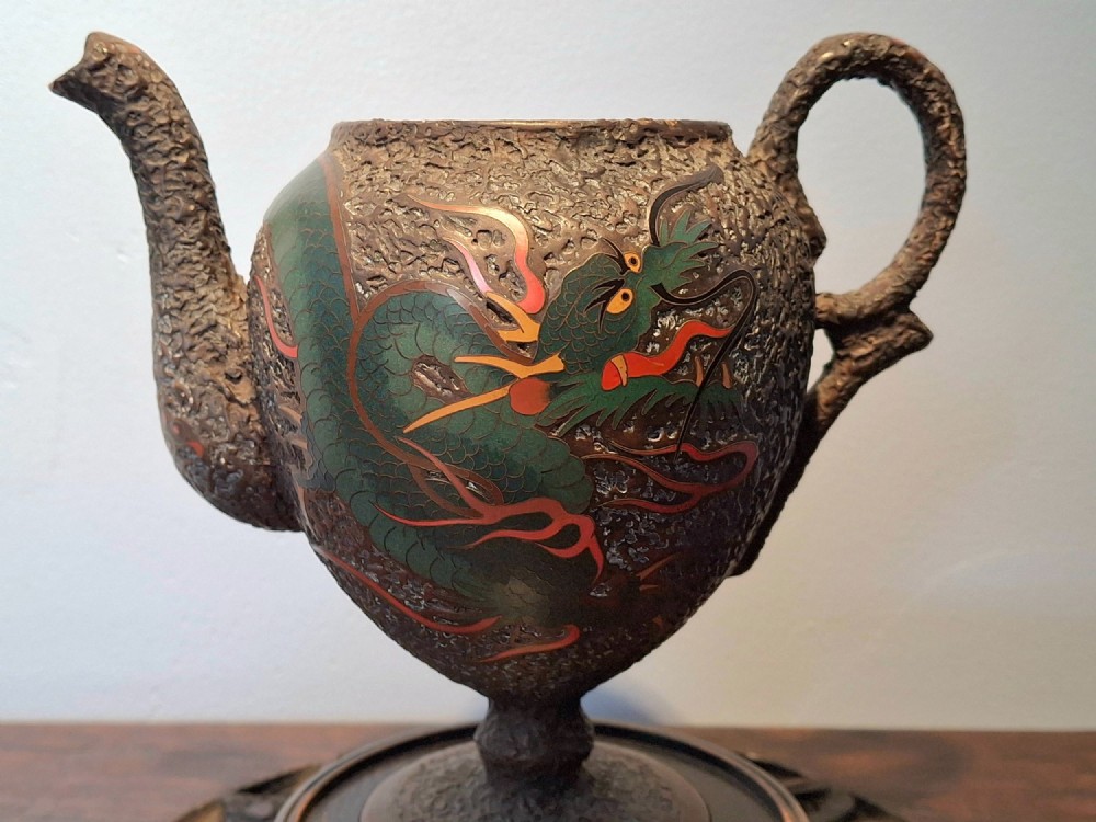 A Japanese Totai Shippo teapot with a textured tree-bark surface and green enamel dragon decoration, resting on a carved wooden base. View III