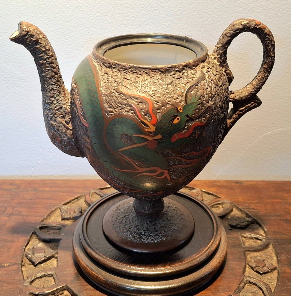 A Japanese Totai Shippo teapot with a textured tree-bark surface and green enamel dragon decoration, resting on a carved wooden base. View IV