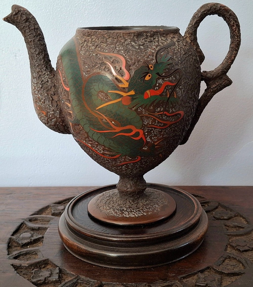 A Japanese Totai Shippo teapot with a textured tree-bark surface and green enamel dragon decoration, resting on a carved wooden base. View V