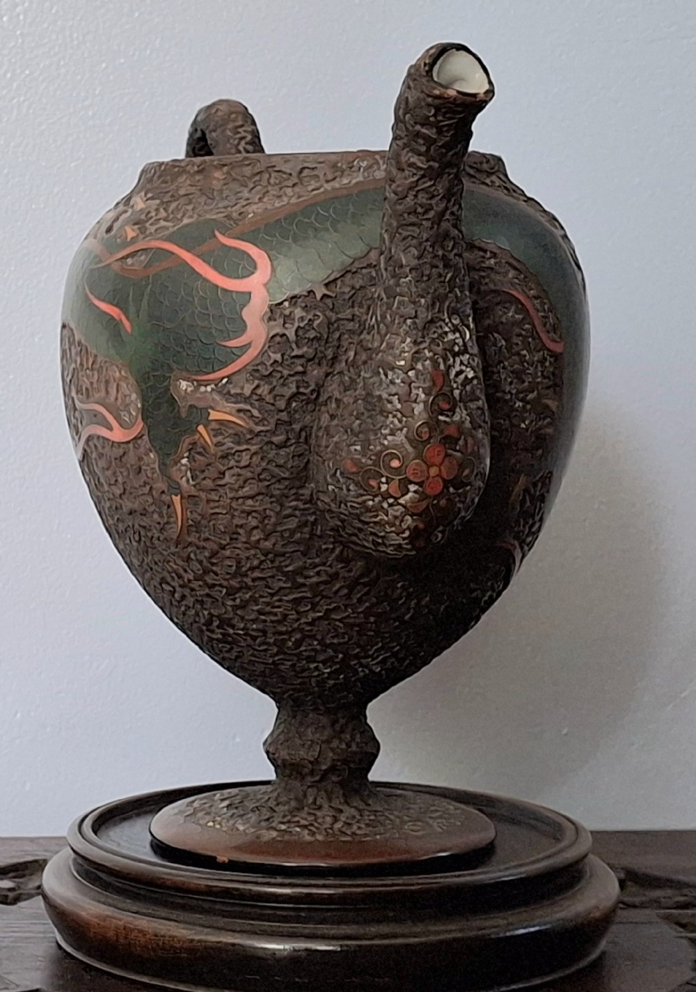 A Japanese Totai Shippo teapot with a textured tree-bark surface and green enamel dragon decoration, resting on a carved wooden base. View VII