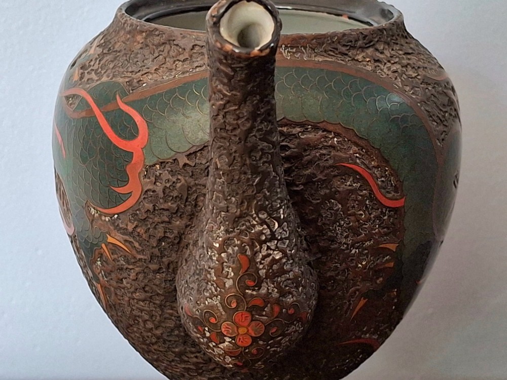 A Japanese Totai Shippo teapot with a textured tree-bark surface and green enamel dragon decoration, resting on a carved wooden base. View XI