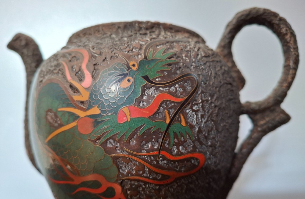 A Japanese Totai Shippo teapot with a textured tree-bark surface and green enamel dragon decoration, resting on a carved wooden base. View XIII