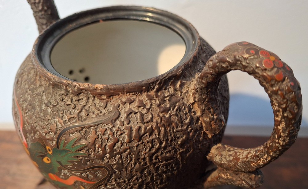 A Japanese Totai Shippo teapot with a textured tree-bark surface and green enamel dragon decoration, resting on a carved wooden base. View XIV