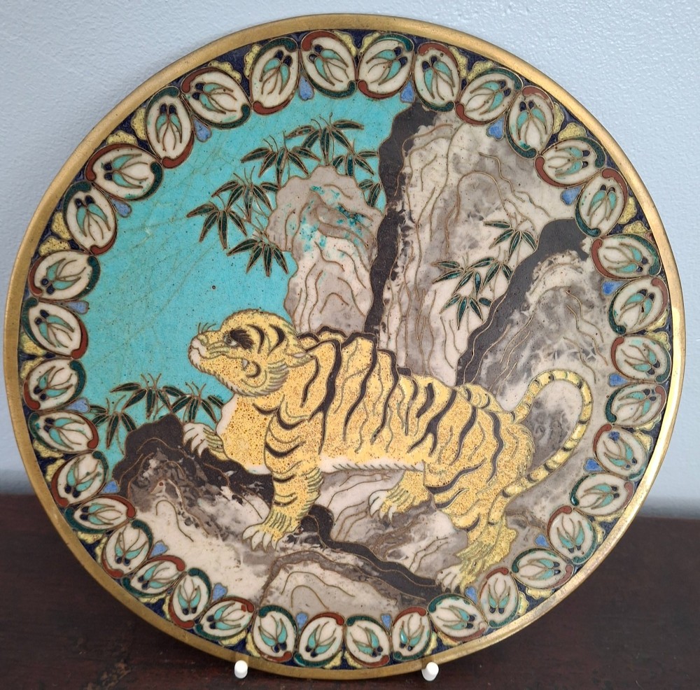 A circular Japanese cloisonne enamel dish depicting a yellow tiger beside bamboo and rocks against a turquoise blue ground with a stylized border.