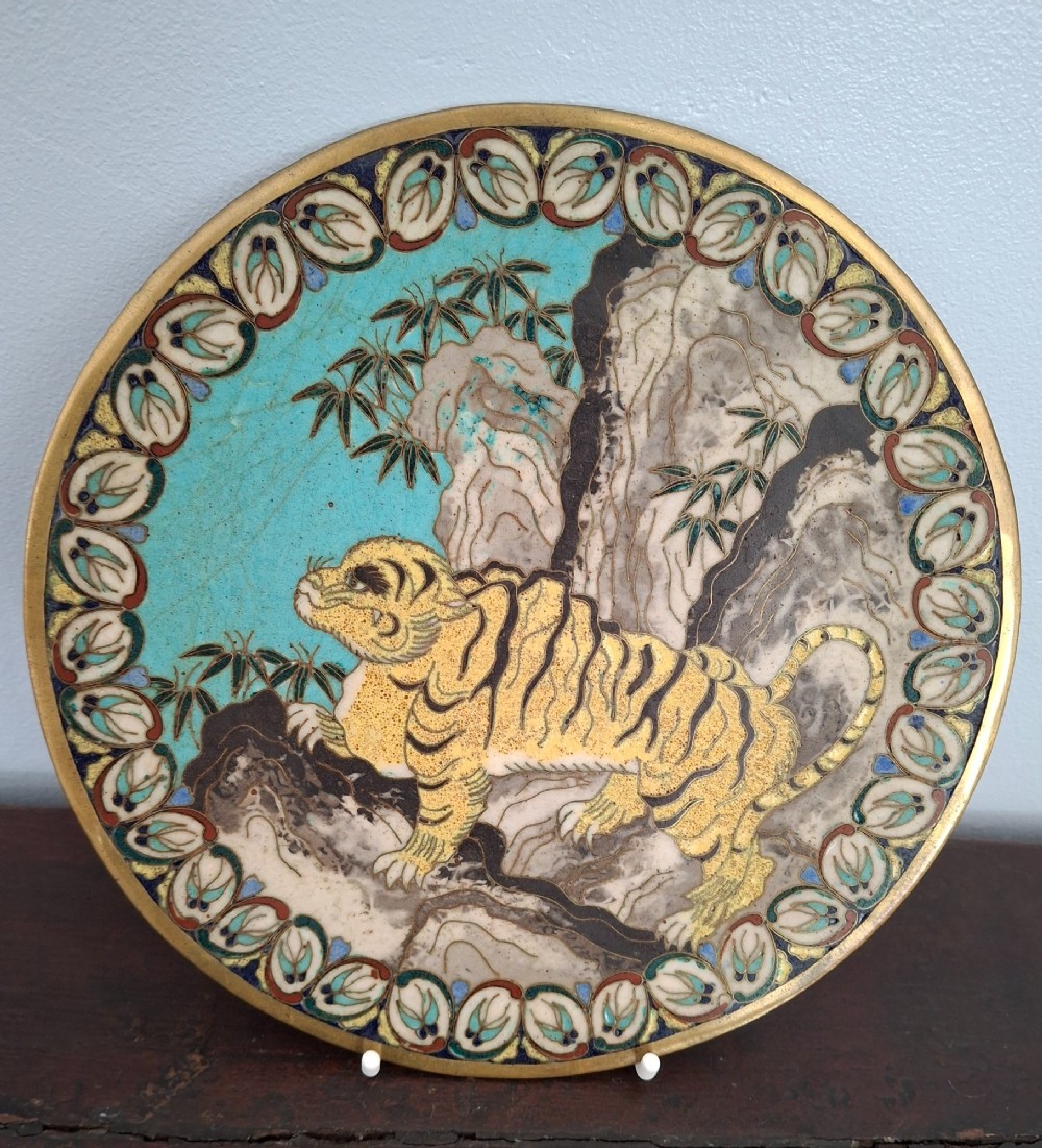 A circular Japanese cloisonne enamel dish depicting a yellow tiger beside bamboo and rocks against a turquoise blue ground with a stylized border. View II