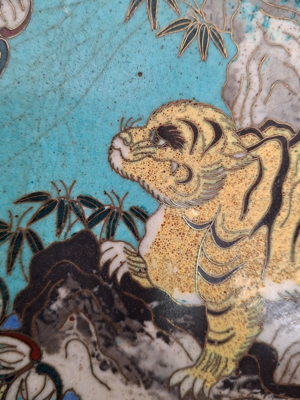 A circular Japanese cloisonne enamel dish depicting a yellow tiger beside bamboo and rocks against a turquoise blue ground with a stylized border. View V