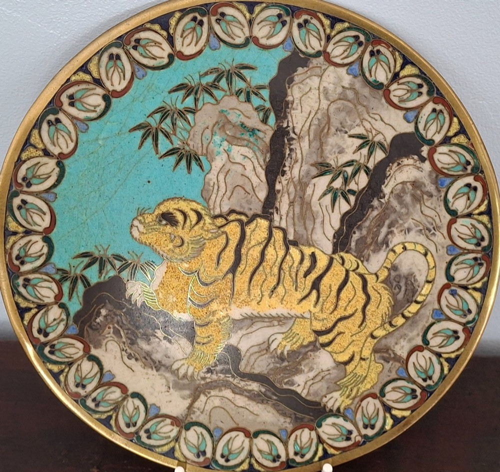 A circular Japanese cloisonne enamel dish depicting a yellow tiger beside bamboo and rocks against a turquoise blue ground with a stylized border. View XI