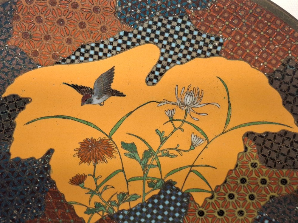 A circular Japanese cloisonne enamel dish featuring a central yellow reserve with a bird and chrysanthemums alongside lotus flowers against geometric mosaic patterns. View IV