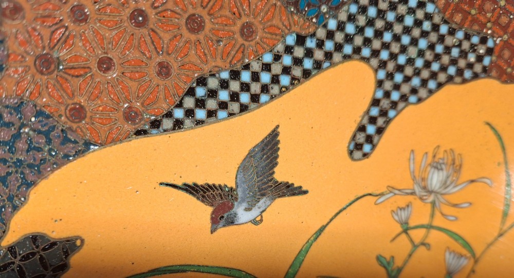 A circular Japanese cloisonne enamel dish featuring a central yellow reserve with a bird and chrysanthemums alongside lotus flowers against geometric mosaic patterns. View VI