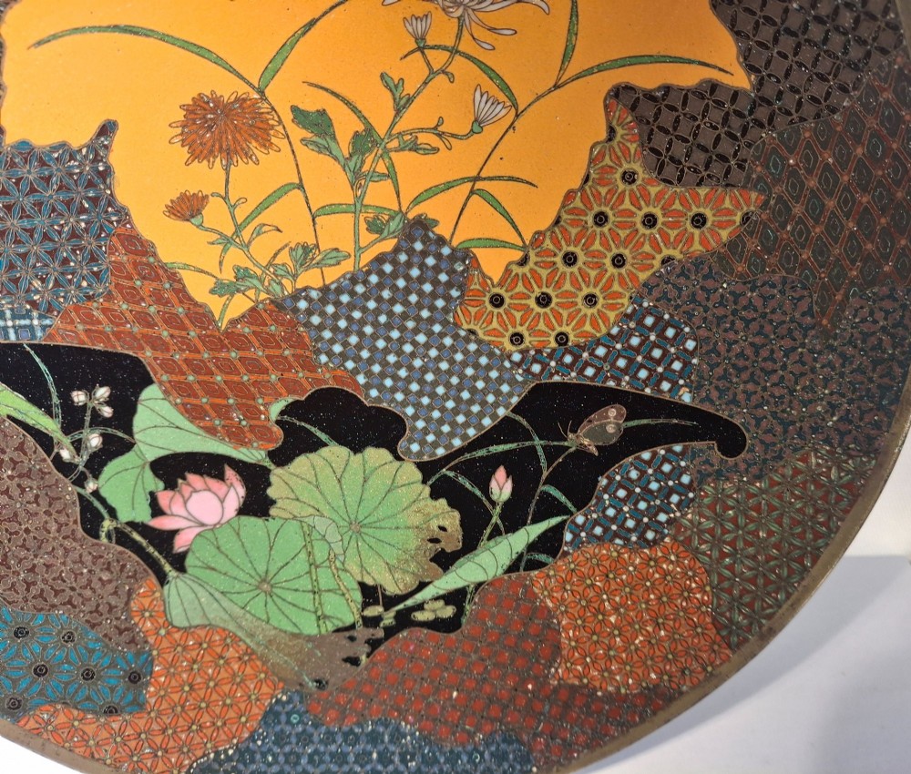 A circular Japanese cloisonne enamel dish featuring a central yellow reserve with a bird and chrysanthemums alongside lotus flowers against geometric mosaic patterns. View VII