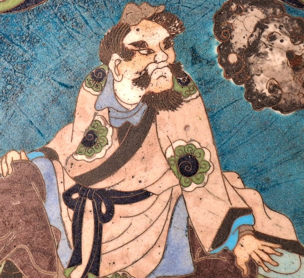 A circular Japanese cloisonne enamel plate depicting a bearded seated figure beside a smoking pot on a turquoise background with a floral border. View V