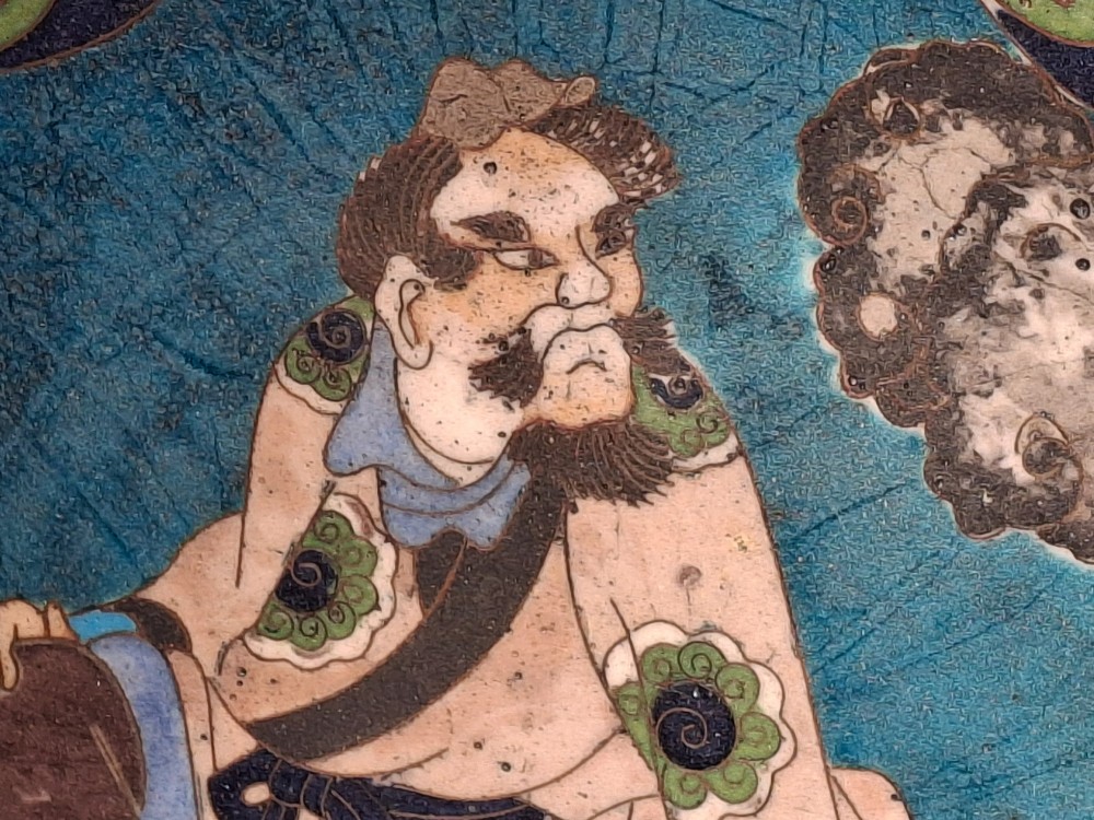 A circular Japanese cloisonne enamel plate depicting a bearded seated figure beside a smoking pot on a turquoise background with a floral border. View VII