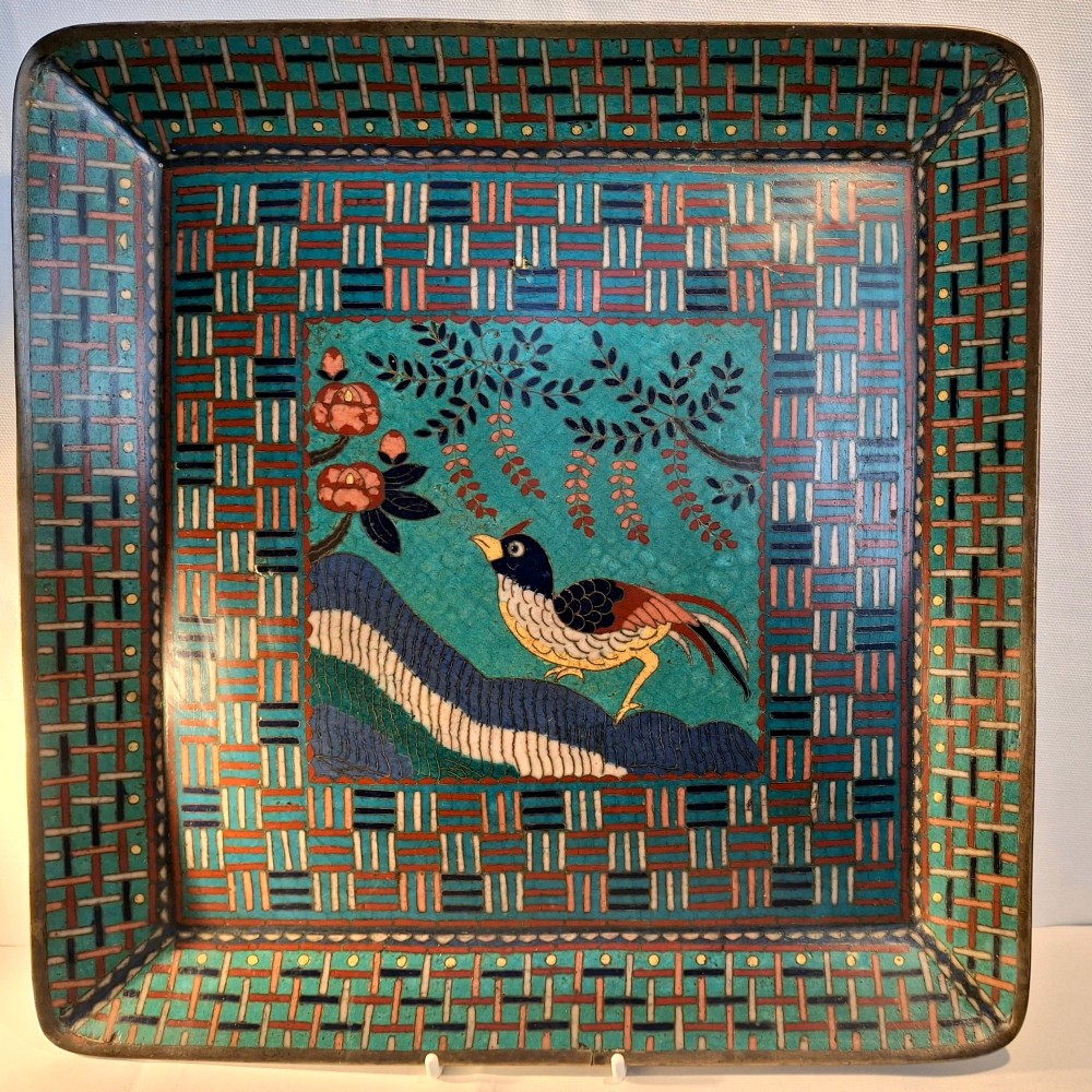 A square Japanese cloisonne enamel tray featuring a central panel with a bird and floral blossoms surrounded by turquoise geometric lattice borders.