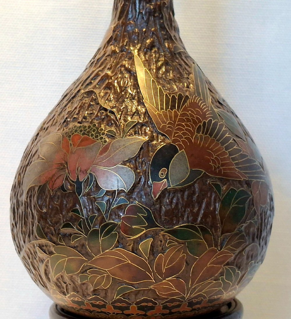 A pear-shaped Japanese Totai Shippo ceramic vase featuring textured brown tree bark enamel with cloisonne bird and floral motifs, resting on a carved dark wood stand. View XII