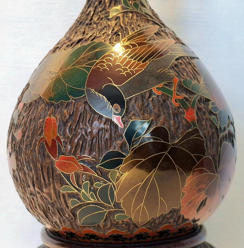 A bulbous Japanese porcelain vase featuring a dark brown tree bark texture decorated with cloisonne enamel birds and foliage on a wooden base. View VII