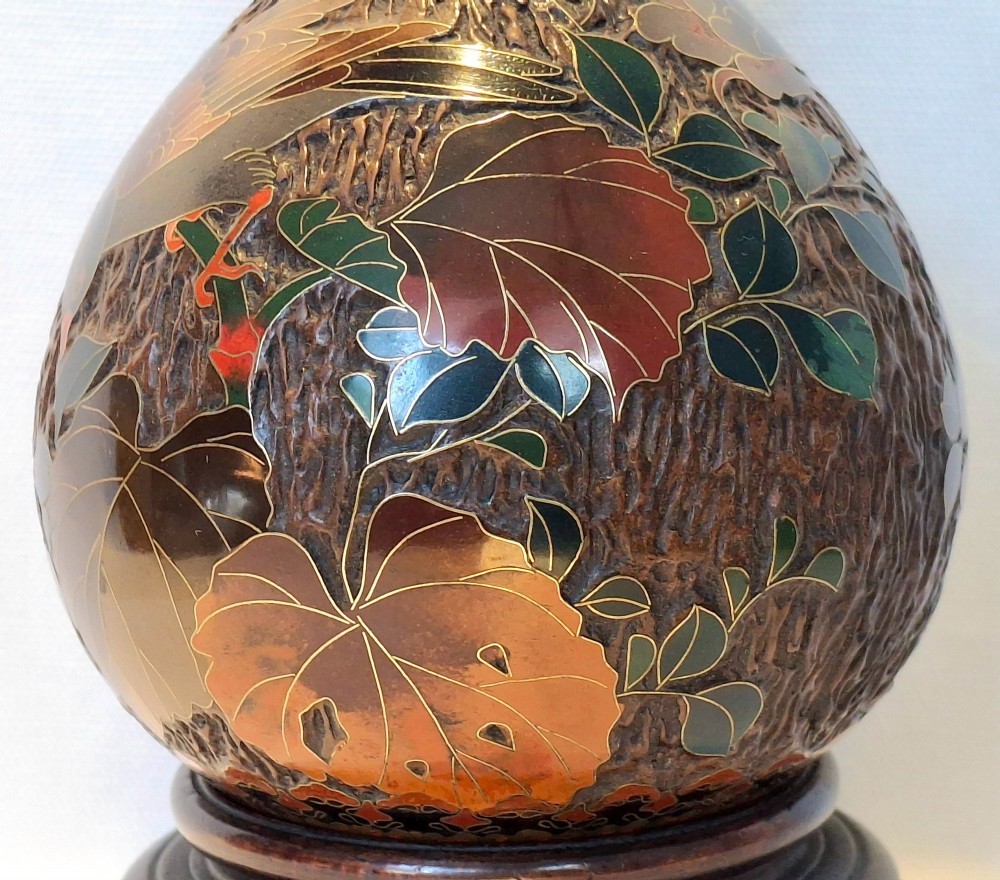 A bulbous Japanese porcelain vase featuring a dark brown tree bark texture decorated with cloisonne enamel birds and foliage on a wooden base. View VIII