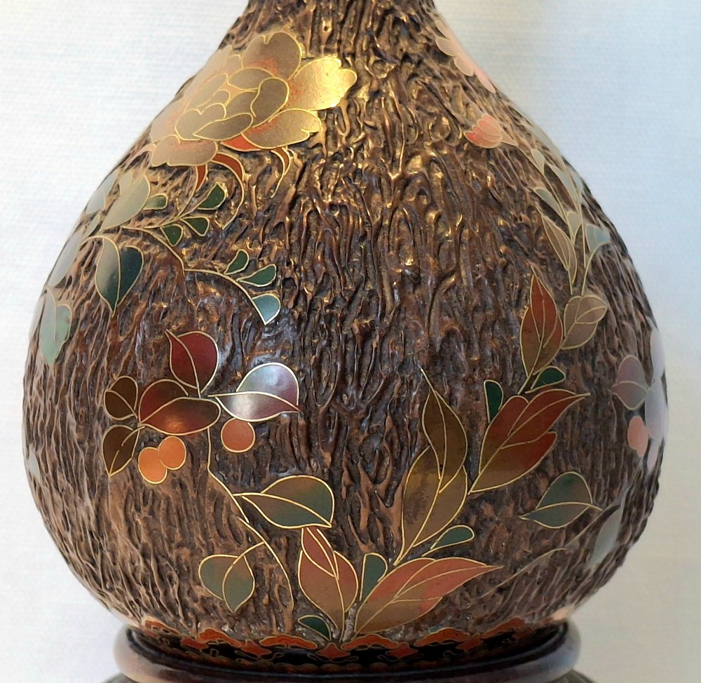 A bulbous Japanese porcelain vase featuring a dark brown tree bark texture decorated with cloisonne enamel birds and foliage on a wooden base. View IX