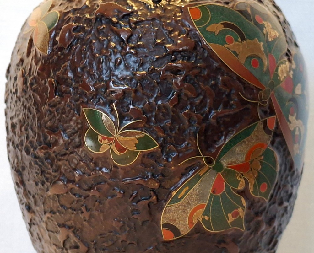 A bulbous dark brown ceramic vase with textured tree-bark surface and colourful enamel butterfly designs resting on a dark carved wooden stand. View IX