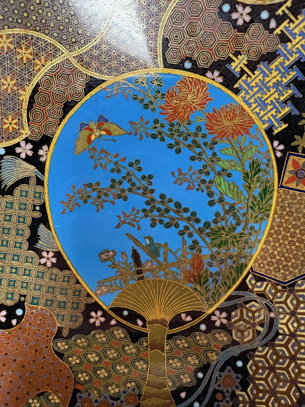A circular Japanese Meiji period cloisonne charger featuring a sky-blue central medallion with chrysanthemums, a butterfly, and a frog, framed by geometric enamel patterns. View V